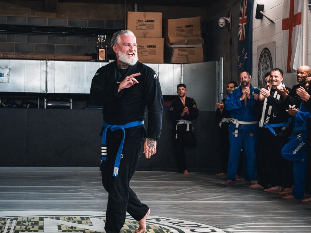 Coach Johnny “Zeus” Tomsett receiving his Brazilian Jiu-Jitsu Purple Belt at New City Martial Arts in Milton Keynes, surrounded by teammates from Southern Tribes BJJ and Team ZR UK.